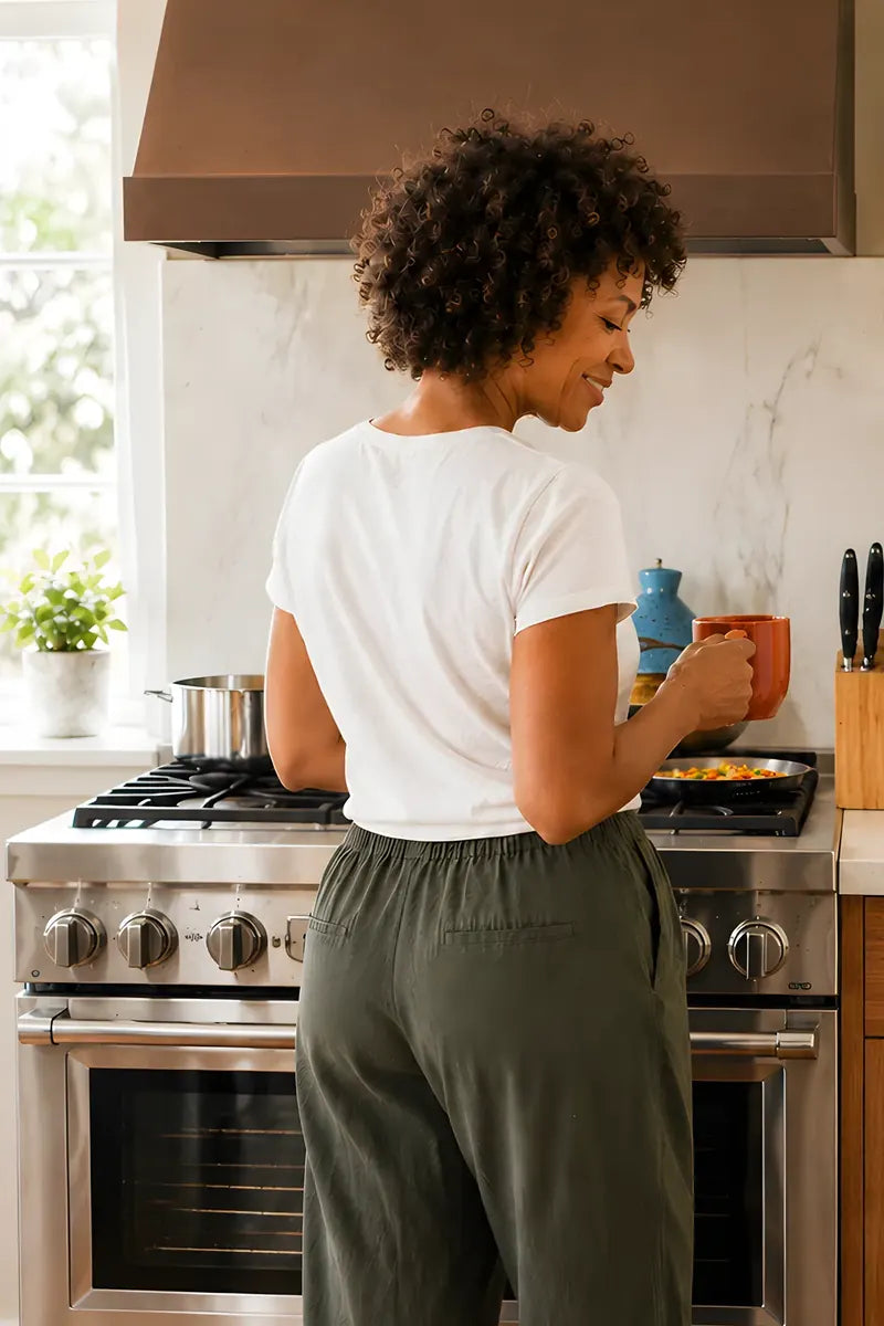A woman at the stove in a bright kitchen in the morning, a mug in her hand