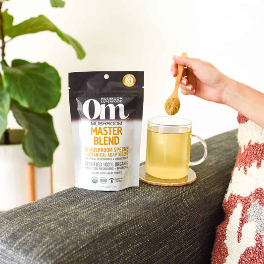 Woman pouring scoop of Om Master Blend powder into glass for mushroom nutrition