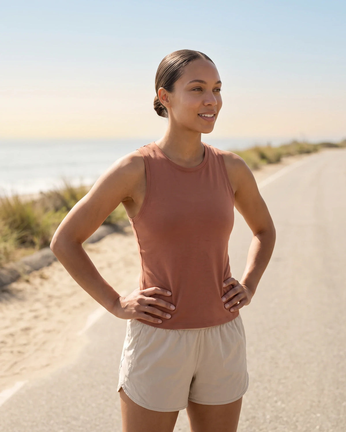 A woman pauses with hands on hips on a coastal path in morning light.