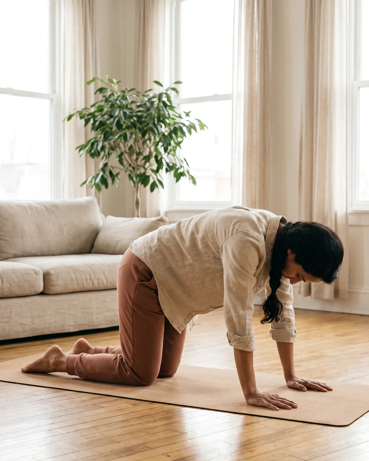 A woman stretches on a mat on the floor of a bright living room.